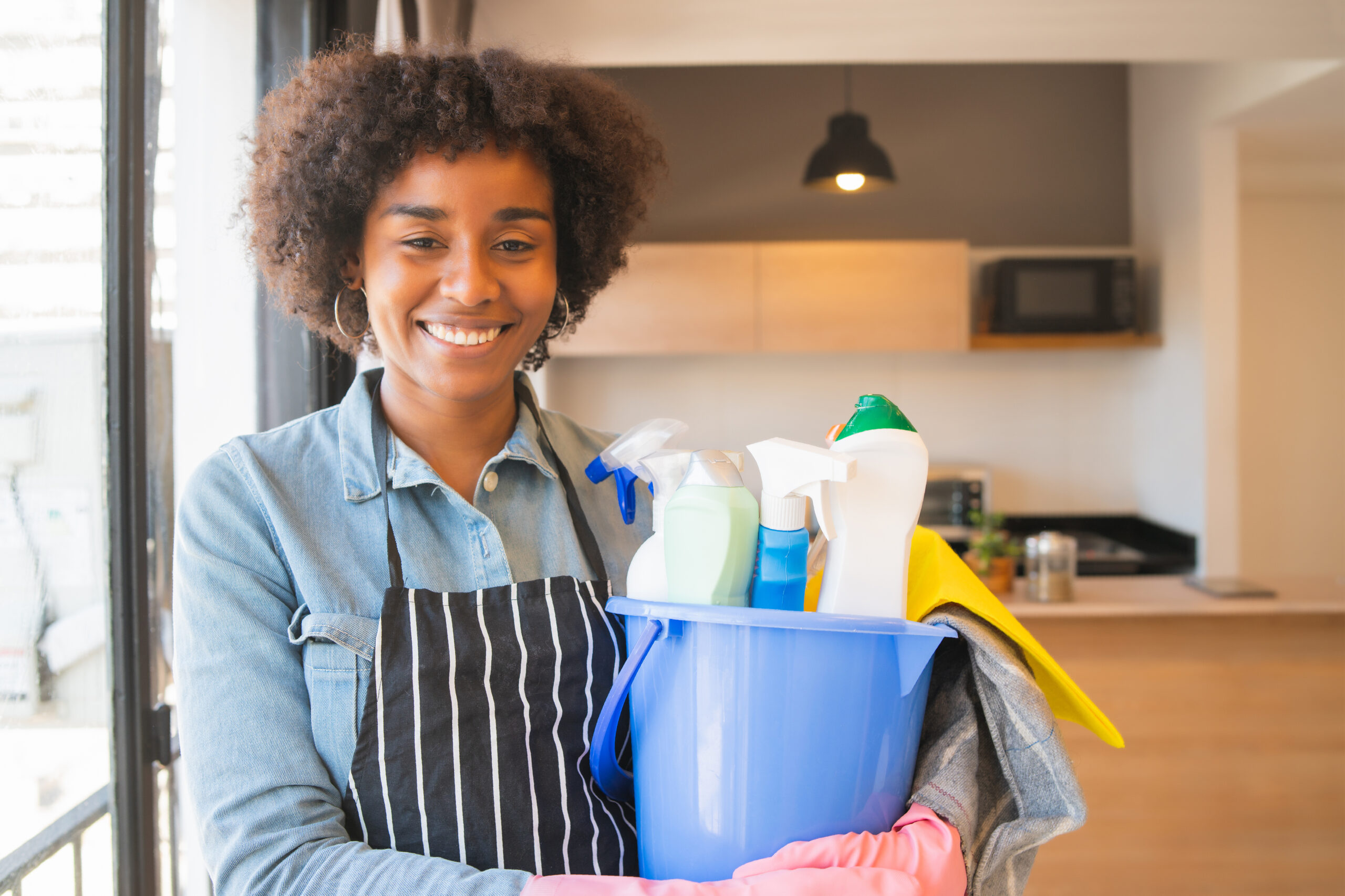 Home afro woman holding a bucket with cleaning items.